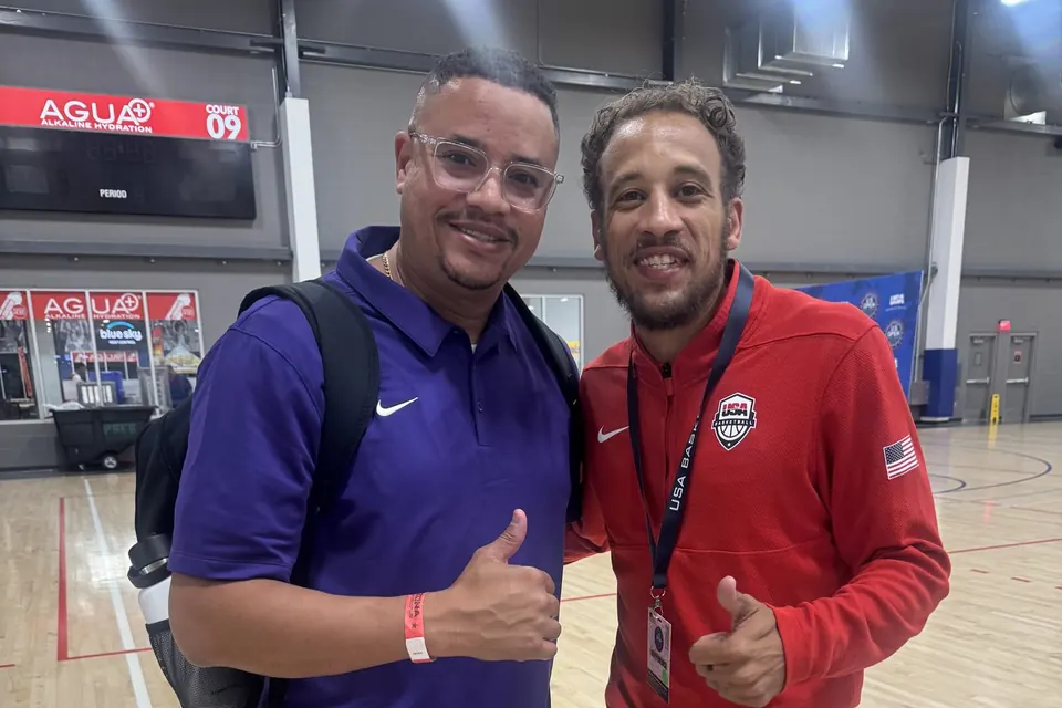 Coach Fish, in a purple polo, standing with a man in USA Basketball apparel at a basketball tournament.