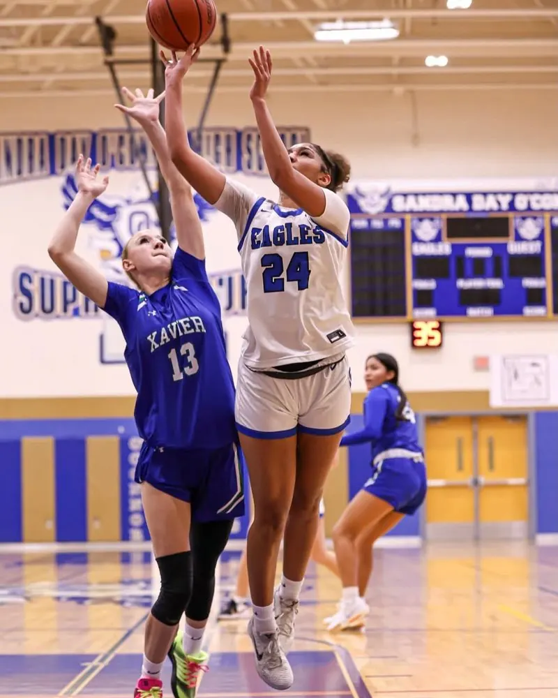 Two high-school girls&rsquo; basketball players contesting a shot at the rim during a game.